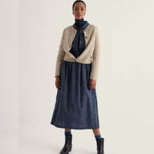 Load image into Gallery viewer, A model stands against a plain light background wearing a cream knit cardigan over a navy blue turtleneck and a matching navy midi skirt, paired with dark ankle boots.