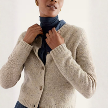 Load image into Gallery viewer, A woman wearing a beige textured knit cardigan over a navy blue turtleneck sweater, shown from the chest up against a plain light background.