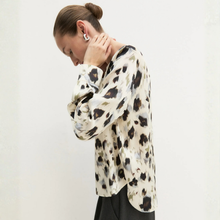 Load image into Gallery viewer, A woman wearing a long-sleeve blouse with an abstract black and gray pattern on a cream background, paired with black trousers, photographed against a plain off-white wall.