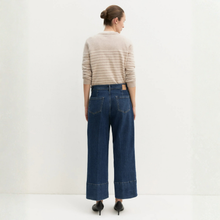Load image into Gallery viewer, A woman shown from the back wearing a beige and white striped long-sleeve sweater, dark blue wide-leg denim jeans, and black pointed-toe heels against a plain white studio background.