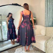Load image into Gallery viewer, Woman trying on a floral dress in front of a mirror in a living room.