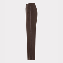 Load image into Gallery viewer, A pair of dark brown trousers shown from the side, featuring a vertical black stripe with white text down the side seam, set against a plain light gray background.