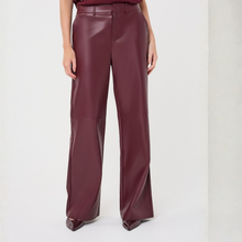 Load image into Gallery viewer, A model wearing high-waisted, wide-leg trousers in a glossy burgundy faux leather material, paired with a matching top and pointed shoes, against a plain light gray studio background.