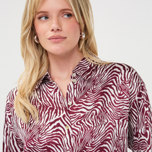 Load image into Gallery viewer, A blonde woman wearing a long-sleeve button-up shirt with a burgundy and white zebra print, photographed against a clean light gray background.