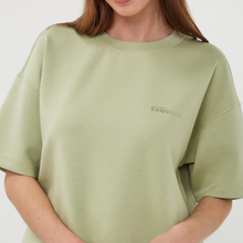Load image into Gallery viewer, Person wearing a green t-shirt with a brand logo on a white background