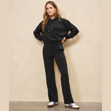 Load image into Gallery viewer, Woman wearing a black outfit with white sneakers against a beige wall