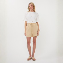 Load image into Gallery viewer, Woman wearing a white top and beige shorts on a white background