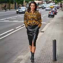Load image into Gallery viewer, Woman in a gold patterned blouse and black leather skirt walking on a city street.