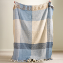 Load image into Gallery viewer, Plaid blanket with blue, beige, and gray colors held up against a neutral background
