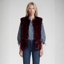 Load image into Gallery viewer, A woman stands against a light gray studio background wearing a sleeveless burgundy faux fur vest over a blue and white striped button-up shirt with embroidered sleeves, paired with dark blue jeans.
