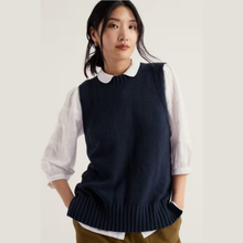 Load image into Gallery viewer, A woman wearing a navy blue ribbed knit sweater vest over a white long-sleeve collared blouse, paired with olive brown pants, set against a plain light beige background.