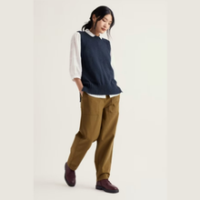 Load image into Gallery viewer, A model wearing a navy blue ribbed knit sweater vest over a white collared shirt, paired with brown trousers and dark burgundy loafers, set against a plain off-white studio background.