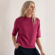 Load image into Gallery viewer, A woman wearing a short-sleeve knit sweater in a rich magenta-pink color, paired with dark trousers, set against a plain off-white studio background.