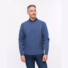 Load image into Gallery viewer, A man wearing a blue knit sweater with vertical textured stripes and a black mock neck collar, paired with dark blue jeans, standing against a plain white studio background.