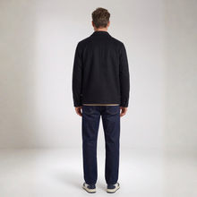 Load image into Gallery viewer, A man viewed from behind wearing a black jacket, navy blue trousers, and white sneakers, standing against a neutral light gray studio background.