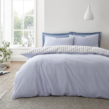 Load image into Gallery viewer, Blue striped bedding set on a bed in a bright bedroom with a window and plant.