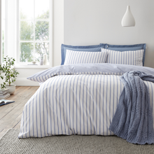 Load image into Gallery viewer, Bed with striped bedding and blue pillows in a bright bedroom.