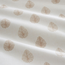 Load image into Gallery viewer, Off-white fabric with a repeating tan leaf pattern, shown with soft folds and shadows.