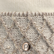 Load image into Gallery viewer, Close-up of a white and grey knitted textile featuring an intricate braided cable design, finished with a round metallic button embellished with a sparkling crystal centre.