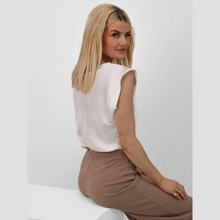 Load image into Gallery viewer, Woman sitting on a white surface wearing a white top and brown pants against a light gray background