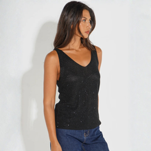 Load image into Gallery viewer, A woman wearing a black sparkly knit V-neck tank top and blue jeans, standing against a plain white wall.