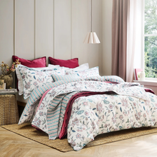 Load image into Gallery viewer, Floral and striped bedding set on a bed in a bedroom with a window and lamp.