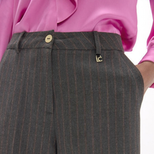 Load image into Gallery viewer, Close-up of a person wearing dark gray pinstriped trousers with a gold button and a small gold logo, paired with a bright pink blouse against a white background.