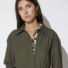 Load image into Gallery viewer, A woman wearing an oversized olive green button-up shirt with a leopard-print inner placket and gold-tone buttons, photographed against a plain light gray background.