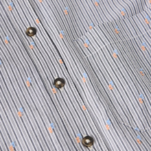 Load image into Gallery viewer, Close-up of a striped button-up shirt fabric with vertical gray and white stripes, small peach and light blue embroidered motifs, and metallic brown buttons.