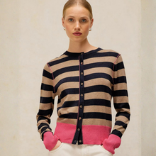 Load image into Gallery viewer, A woman wearing a striped cardigan sweater with navy and beige horizontal stripes, a bright pink hem, and pink ribbed cuffs, paired with white pants against a neutral beige background.