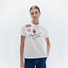 Load image into Gallery viewer, A woman modeling a white short-sleeve t-shirt with 'Made in Lofa' and brand patches on the front, paired with dark blue jeans against a clean white studio background.