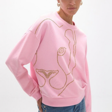 Load image into Gallery viewer, A woman wearing a light pink crewneck sweatshirt decorated with gold rhinestone outlines of mermaid tails and a wave-like pattern, paired with blue jeans against a plain white background.