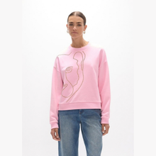 Load image into Gallery viewer, A woman modeling a light pink crewneck sweatshirt with a large abstract face design outlined in gold rhinestones, paired with blue jeans against a plain white background.