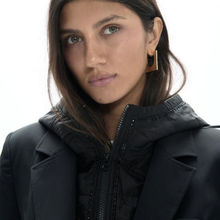 Load image into Gallery viewer, A close-up shot of a woman wearing a black hooded puffer jacket and a black geometric earring against a plain white background.