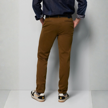 Load image into Gallery viewer, A person shown from the back wearing slim-fit brown chino pants, a dark blue denim shirt, and sneakers, standing against a light gray studio background.