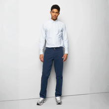 Load image into Gallery viewer, A male model stands against a light gray studio wall wearing a light blue long-sleeve button-up shirt, navy blue trousers, and silver sneakers.