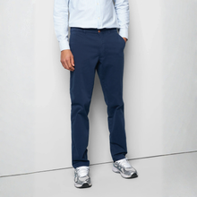 Load image into Gallery viewer, A person wearing navy blue slim-fit trousers, a light blue and white striped long-sleeve shirt, and silver sneakers, standing against a light gray wall.