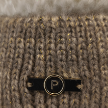 Load image into Gallery viewer, Close-up of a chunky knit winter hat in taupe-brown with subtle gold flecks, featuring a black and gold circular metal bar with a letter 'P' logo.