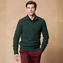 Load image into Gallery viewer, A man wearing a dark green quarter-zip knit sweater over a collared shirt and burgundy trousers, standing against a warm beige textured studio background.