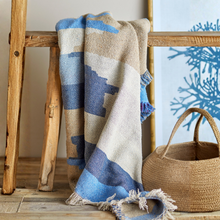 Load image into Gallery viewer, Blue and beige patterned blanket draped over a wooden stool with a woven basket in the background.