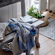 Load image into Gallery viewer, Blue and gray blanket draped over a wooden bench in a cozy room with plants and a guitar.