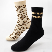 Load image into Gallery viewer, Two crew socks on a white background: one black sock with beige leopard-print bands near the cuff, and one cream sock with brown leopard spots across the foot.