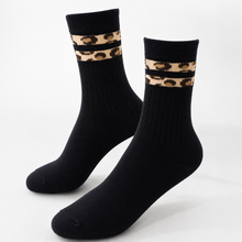 Load image into Gallery viewer, A pair of black crew socks with a leopard print pattern band near the top, displayed on a clean white background.