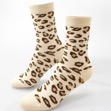 Load image into Gallery viewer, A pair of crew socks with a leopard print pattern in brown and tan on a cream background, displayed against a plain white studio background.