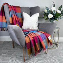 Load image into Gallery viewer, Gray armchair with a colorful plaid blanket and white pillow, next to a small table with flowers.