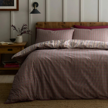 Load image into Gallery viewer, A bed dressed in a red and white gingham check duvet cover and matching pillowcases, styled in a bedroom with a wooden headboard, bedside table, wall sconce, and neutral paneled wall.