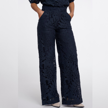Load image into Gallery viewer, A person wearing high-waisted, wide-leg trousers in a dark navy blue floral lace or embroidered fabric, paired with a matching top, shown against a plain light gray studio background.