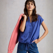Load image into Gallery viewer, Model posing with pink sweatshirt along with wearing the White Stuff Nicole Linen Blend Top in Bright Blue, with a grey background.