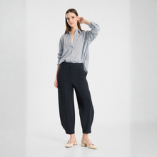 Load image into Gallery viewer, A woman modeling a blue and white vertically striped button-down shirt with dark navy wide-leg trousers and beige flat shoes, standing against a light gray studio background.