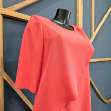 Load image into Gallery viewer, Coral dress on a mannequin against a geometric-patterned wall.